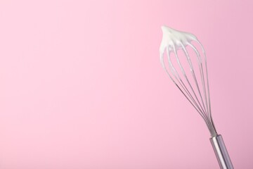 Whisk with whipped egg whites on pink background, space for text
