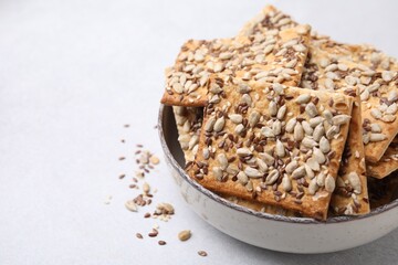 Cereal crackers with flax, sunflower and sesame seeds in bowl on light textured table, closeup. Space for text