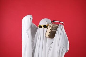 Person in ghost costume and sunglasses using retro radio receiver on red background