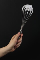 Woman holding whisk with whipped cream on black background, closeup