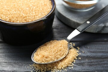 Brown sugar in bowl and spoon on black wooden table, closeup