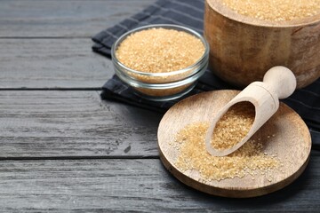 Brown sugar in bowls and scoop on black wooden table. Space for text