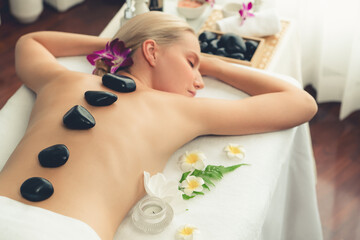 Obraz na płótnie Canvas Hot stone massage at spa salon in luxury resort with day light serenity ambient, blissful woman customer enjoying spa basalt stone massage glide over body with soothing warmth. Quiescent