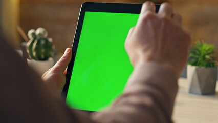 Hand scrolling greenscreen tablet searching information in home office close up
