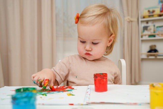 Child baby toddler girl paints with finger paints and gets her hands dirty