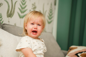 Fototapeta premium The toddler child is crying and screaming with a red face at home