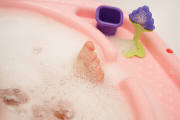 A cute baby's leg is bathed in foam in a bathtub