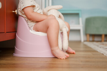 Child toddler baby sits on a pink pot and holds a bunny,baby's feet