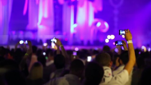 Crowd of people raising their hands up with phones and filming on dance musical show.