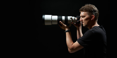 young photograph aiming with camera and big white lens isolated on black background