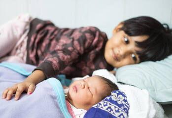 South asian little girl is watching her newborn sister with love and affection 