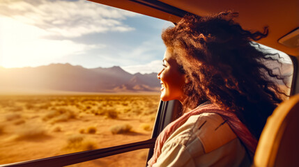 Woman looking out the window of vehicle in desert area with mountains in the background.