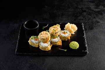 Salmon tempura roll on a textured black slate with condiments