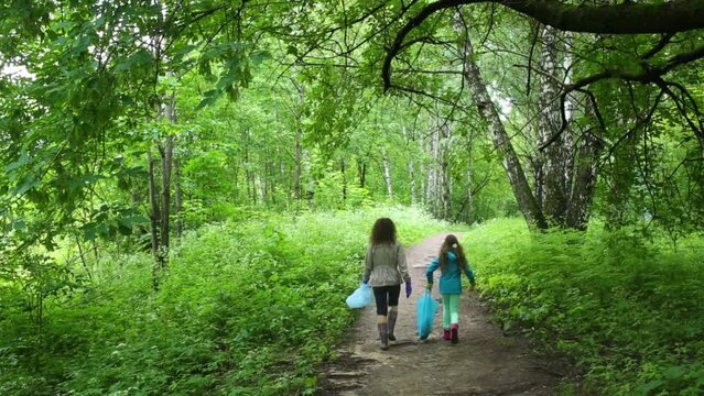 Mother and her daughter are walking with a plastic bags on the forest