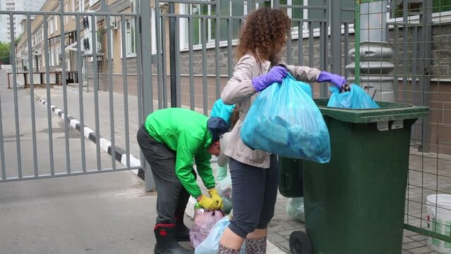 Mother is putting trash to the trashcan with her children.