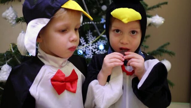 Two little boys in a penguin costume are standing near christmas tree