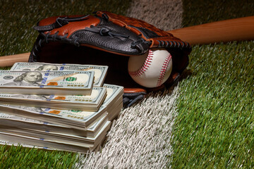 Baseball in mitt with bat on grass field with piles of one hundred dollar bills