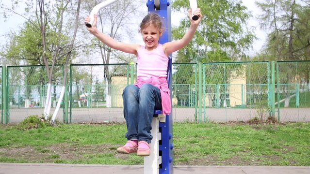 Girl raising herself sitting on street exerciser pushing up handle.