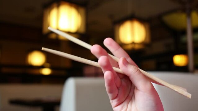 Childs hand with chopsticks inside sushi restaurant with tables
