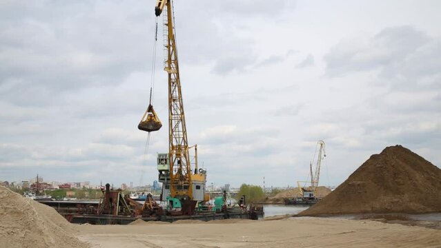 Crane at dock on Volga River pouring pile of earth bucket.