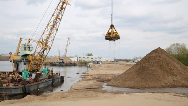 Crane on platform in water of Volga River dragging earth bucket mound hill.