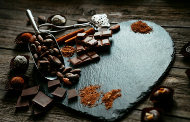 Handmade candies, two truffles, cocoa powder, chocolate and other lay on heart stone shape. Sweet delicious things on old wood background.