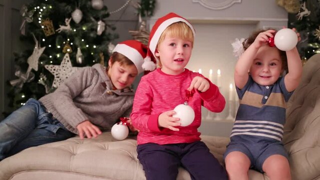 Three children in santa caps sit on couch with balls
