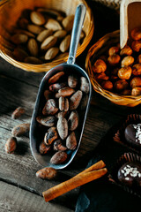 Metal scoop with cocoa beens beside small baskets with nuts on wood stand.	