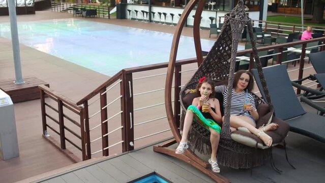 Mother and daughter are sitting on lounge, drinking juice from straw