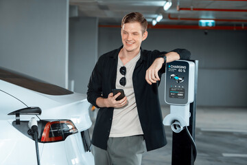 Young man travel with EV electric car to shopping center parking lot charging in downtown city...