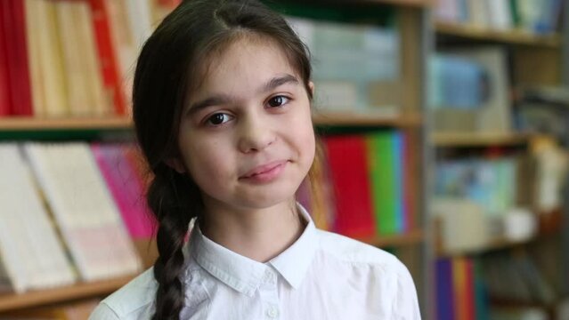 Girl with pigtail and a white blouse in the library at the book shelves