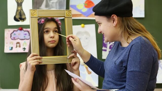 Two girls pretending that paint a portrait in a frame in the classroom