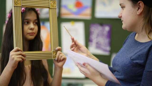 Two girls in the classroom, one paints a portrait of another