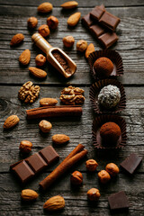 Handmade candies, two truffles with cocoa powder and one with coconut flakes. Chocolate candies inside of candy wrapper on wood table stand with nuts