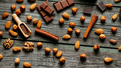 Chocolate, cinnamon, almonds, walnuts and hazelnuts on wood table. Horizontal background
