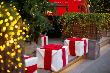 White gift boxes with red bows on a background of wooden tubs with junipers in the Christmas lights