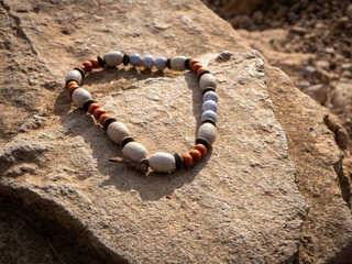 Forgotten surfer necklace or bracelet made of wooden beads lies on sandstone under sunlight