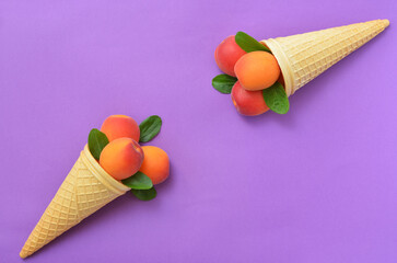 two waffle cones with ripe apricots on a purple background