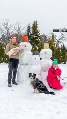 Fototapeta na wymiar family and their pet dog enjoying a winter day with a homemade snowman family in the yard surrounded by snowy trees