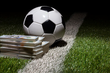 Soccer ball on grass field with stripe by stacks of one hundred dollar bills
