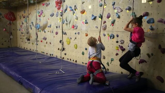 Two girls in the climbing gym trying to raise one of them on a rope
