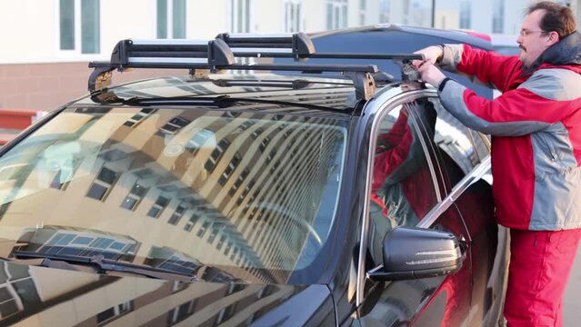 A man attaches to the car roof rack in the yard at sunny day