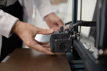 Close up shot of unrecognizable male hands arranging 3D printer extruder above metal print bed