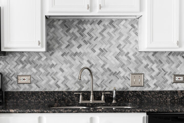 A kitchen faucet detail with white cabinets, a marble herringbone tile backsplash, and granite...
