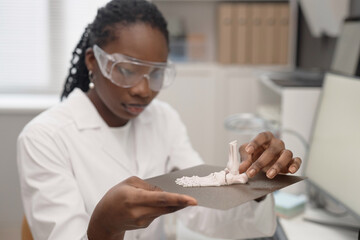 Medium shot of defocused African American female technician in safety glasses holding metal hot bed...