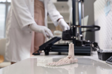 Close up shot of produced white-colored 3D dental and bone samples on acrylic print bed in laboratory, unrecognizable technician working in blurred background