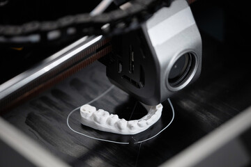 Macro shot of 3D printer extruder producing white-colored human lower jaw bone sample in...