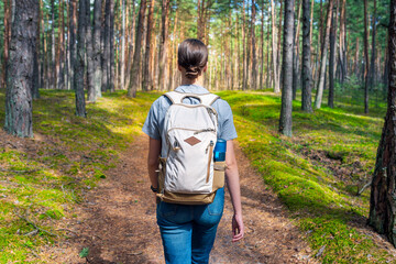 A young woman with a backpack walks through the forest. Hiking in the woods. - 718322539