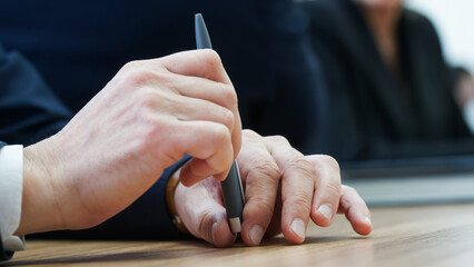 Man holds a fountain pen with his fingers while sitting at his desk during a business meeting....