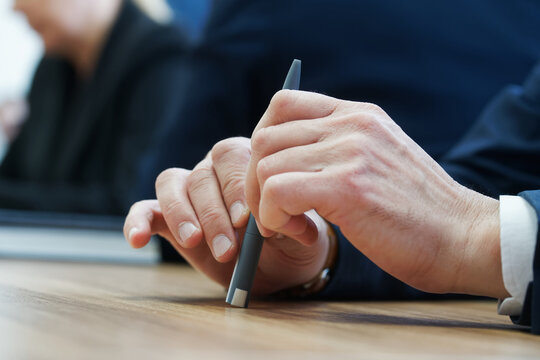 A man holds a pen in his hand during a business meeting or negotiation. Sitting at a desk, anonymous, unrecognizable, no face. Photo. Selective focus